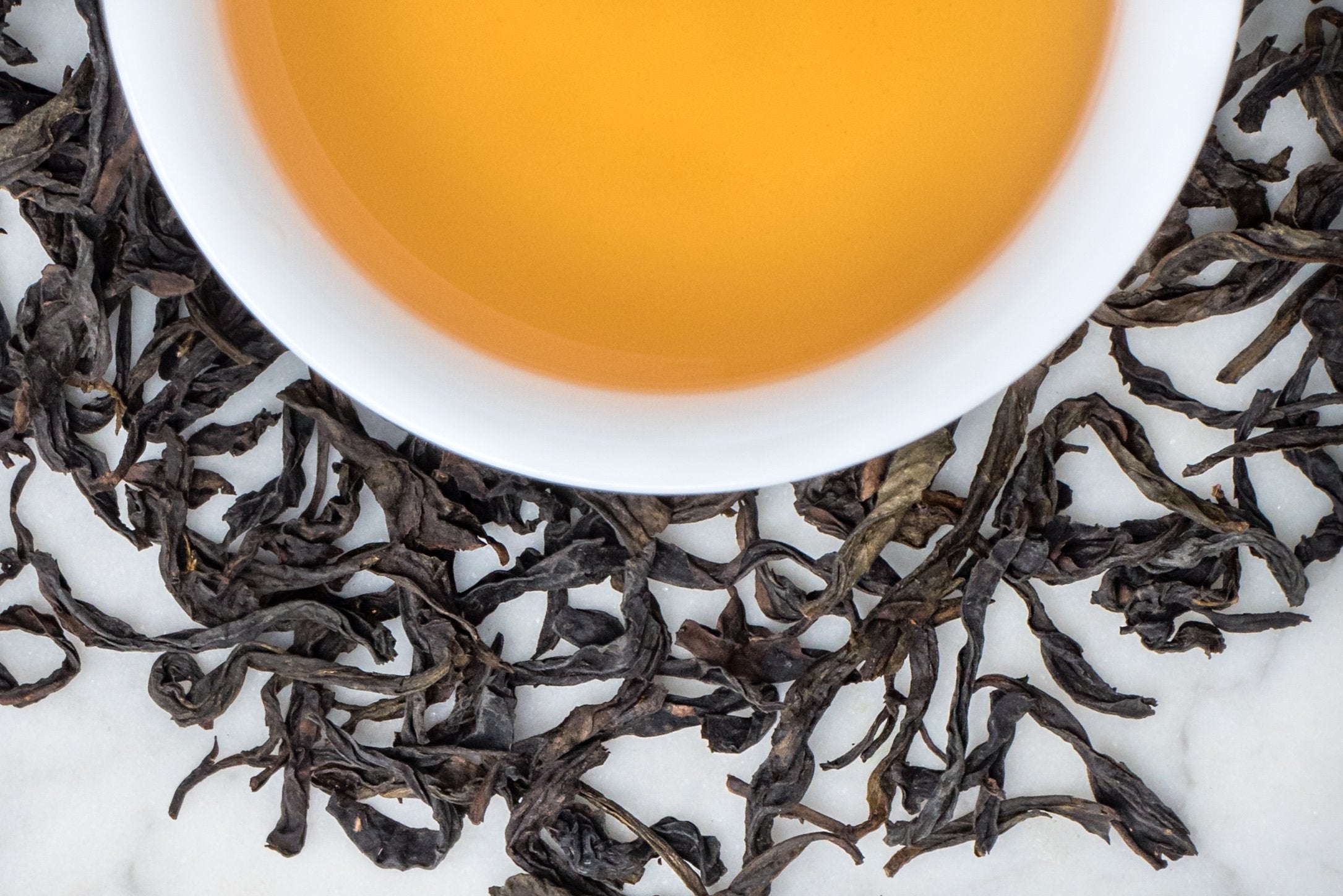 Qi Lan Wuyi oolong leaves and brewed tea. Large, dark brown twisted leaves surround a cup of amber-colored brewed tea.