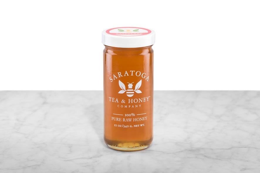 Amber-hued Raspberry Blossom Honey displayed in a 12oz cylindrical glass jar with a white lid. The logo and the words: "100% Pure Raw Honey" are printed on the jar.