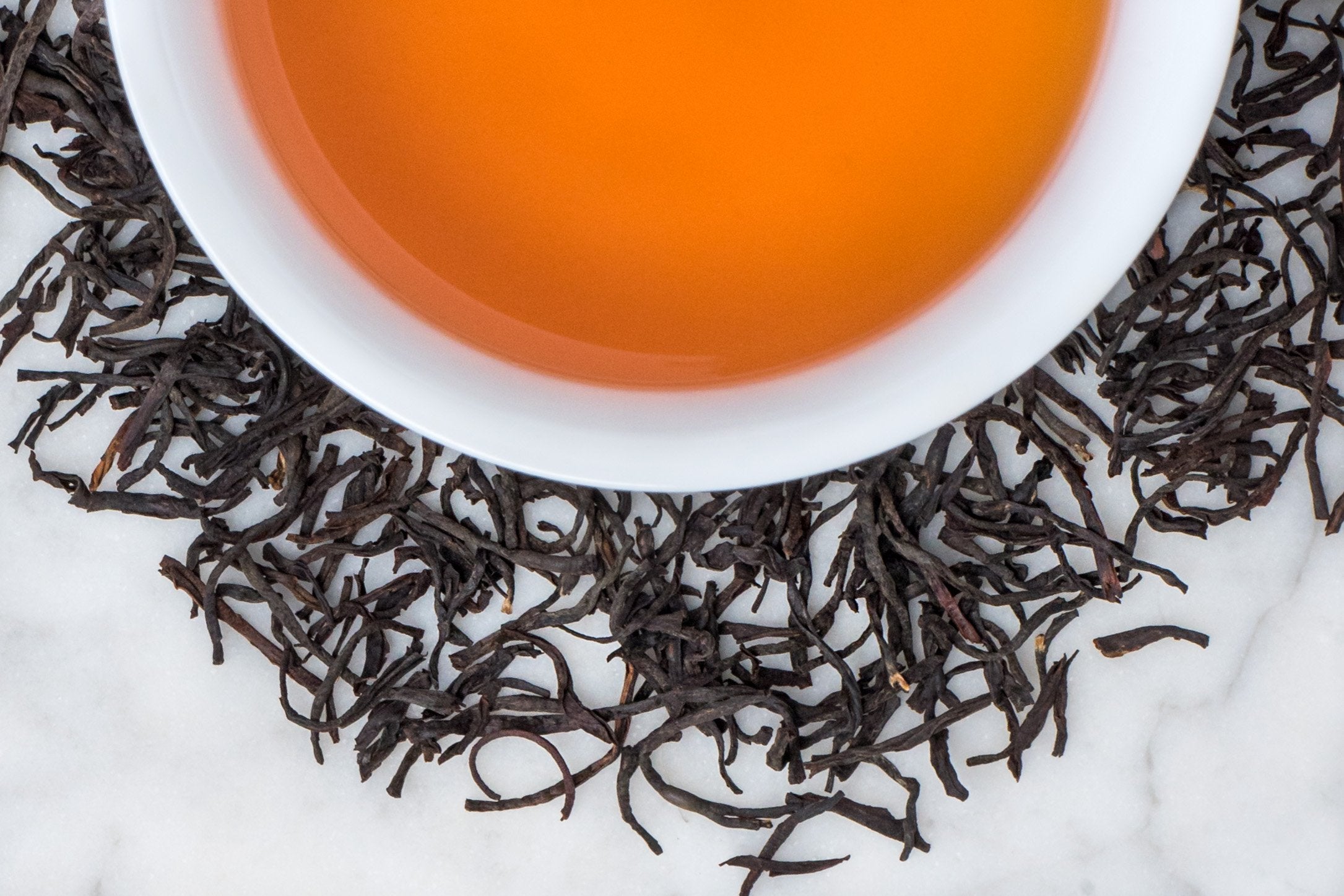 Rwanda Rukeri leaves and brewed tea. Long, twisted black tea leaves surround a cup of russet-hued brewed black tea. 