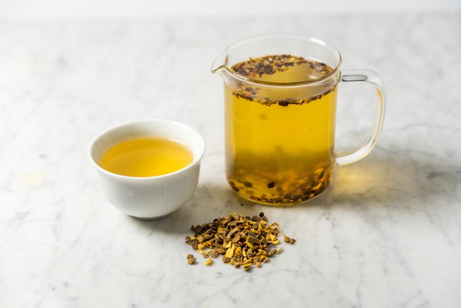 Fountain of Youth turmeric tea infused and presented in a white cup beside a glass infuser
