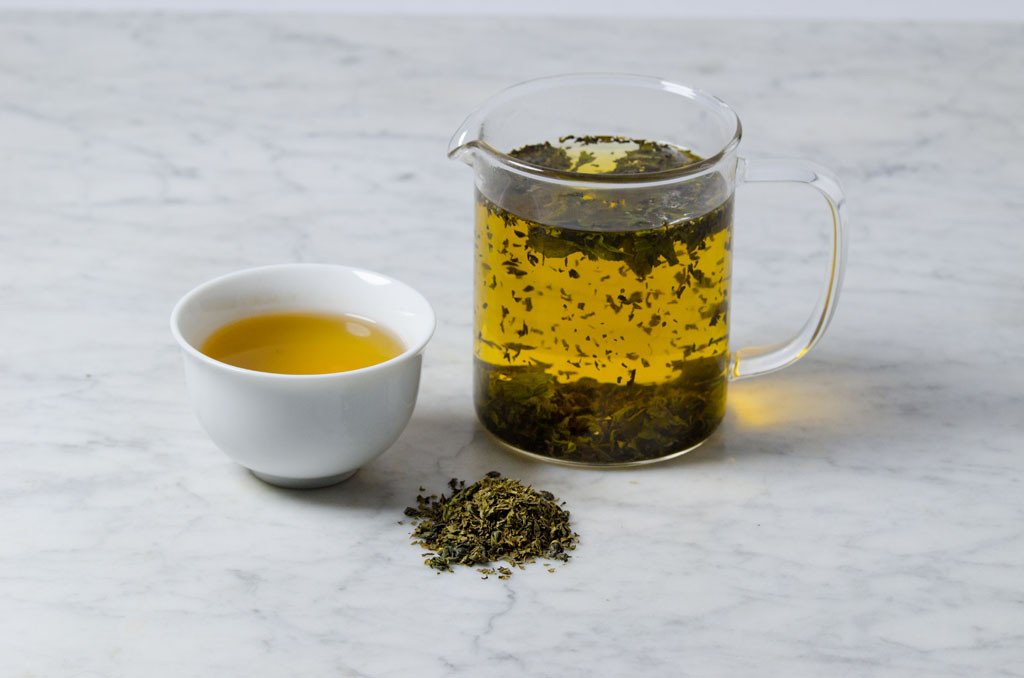 loose leaf mint green tea infused in a glass beaker and white cup