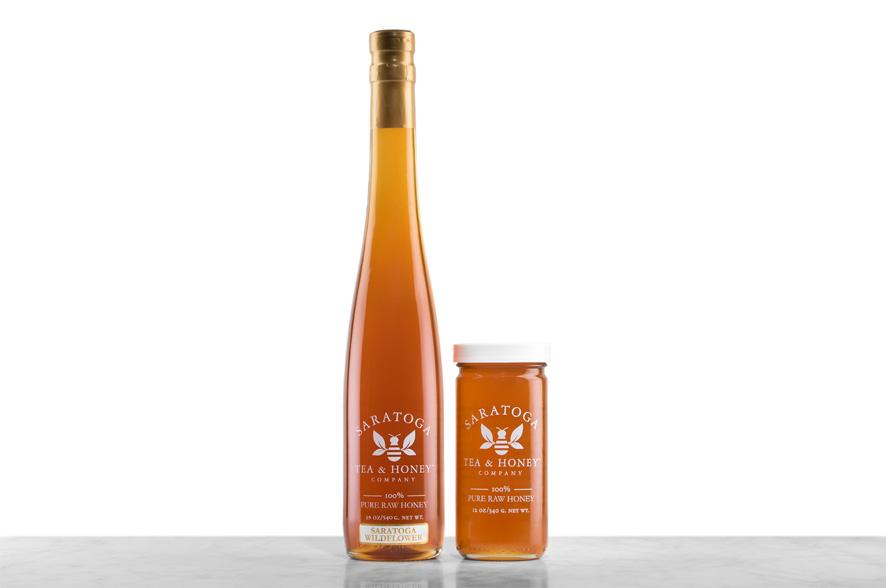 Amber-hued Saratoga Springs Wildflower Honey displayed in two glass jars with the logo and the words: "100% Pure Raw Honey". Left: Tall, 19oz bottle shaped like a wine bottle and capped with a cork. Right: 12oz cylindrical bottle with white cap. 