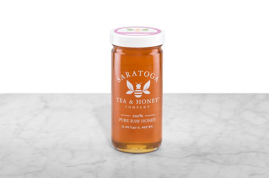 Amber-hued Saratoga Springs Wildflower Honey displayed in a 12oz cylindrical glass jar with a white lid. The logo and the words: "100% Pure Raw Honey" are printed on the jar.