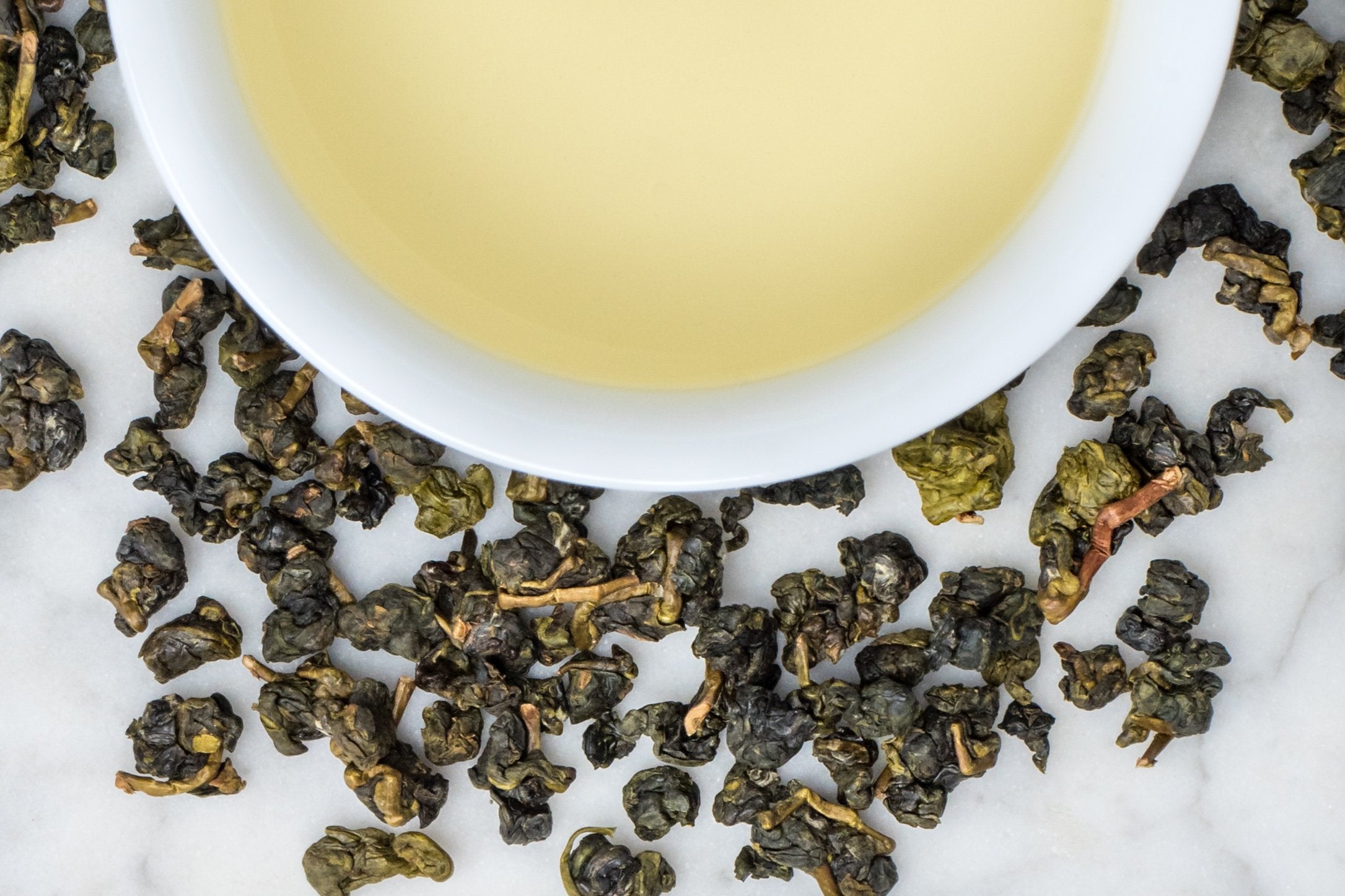 Shan Lin Xi leaves and brewed tea. Rolled, lightly oxidized oolong leaves surround a cup of pale-gold brewed tea.