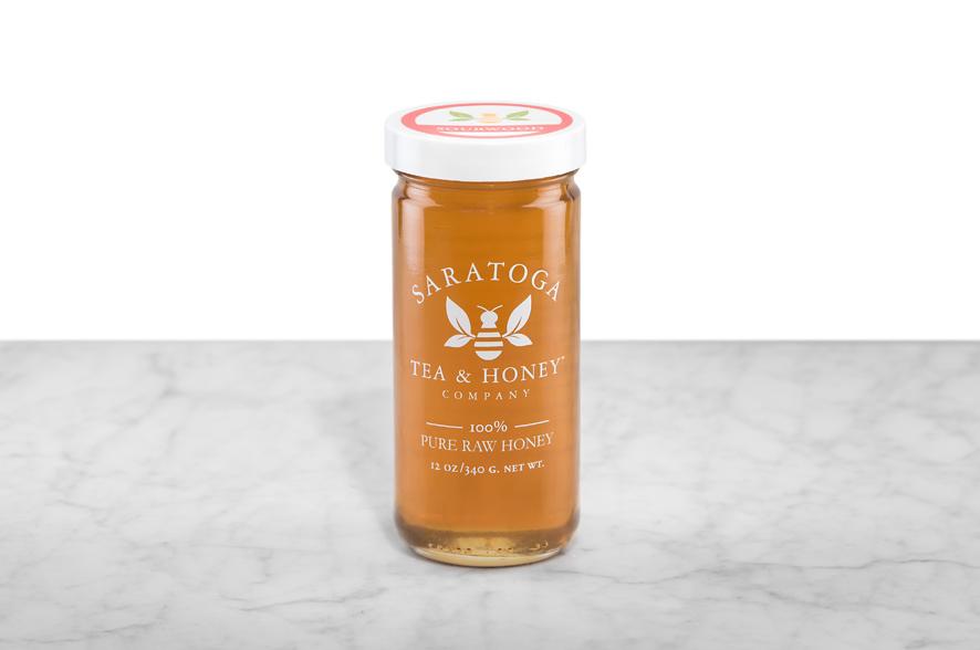 Amber-hued Sourwood Honey displayed in a 12oz cylindrical glass jar with a white lid. The logo and the words: "100% Pure Raw Honey" are printed on the jar.