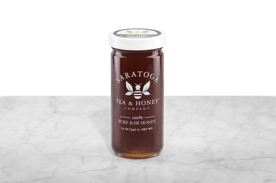 Dark brown Spanish Black Forest Honey displayed in a 12oz cylindrical glass jar with a white lid. The logo and the words: "100% Pure Raw Honey" are printed on the jar.