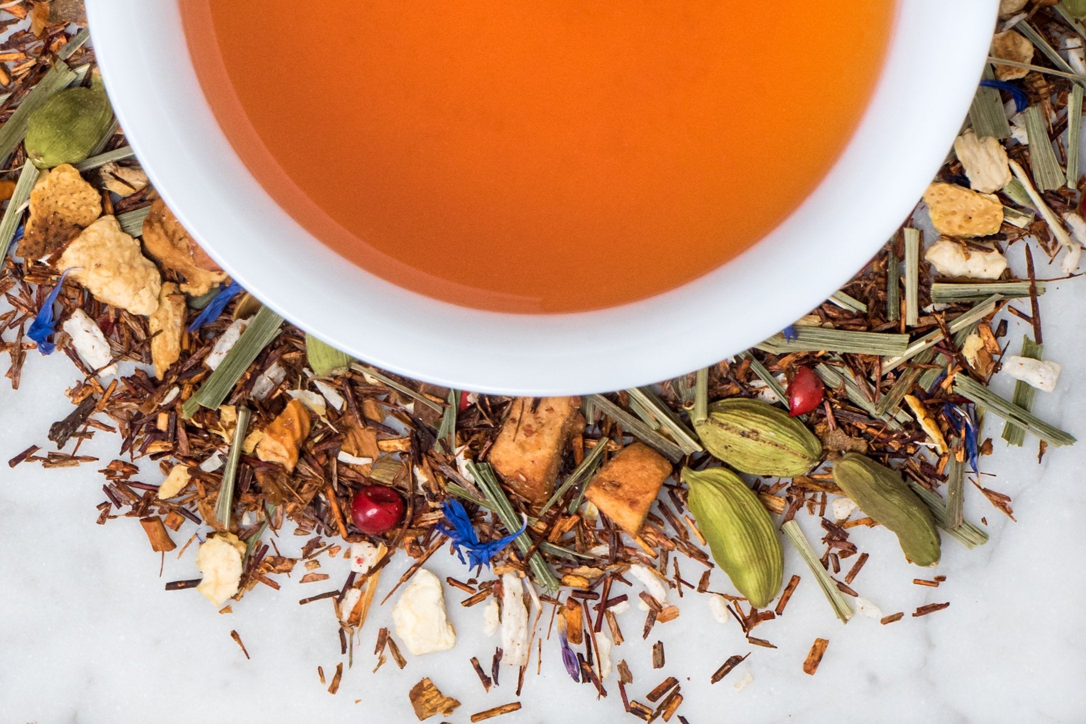 loose leaf rooibos and citrus herbal tea surrounding a white cup with brewed tea