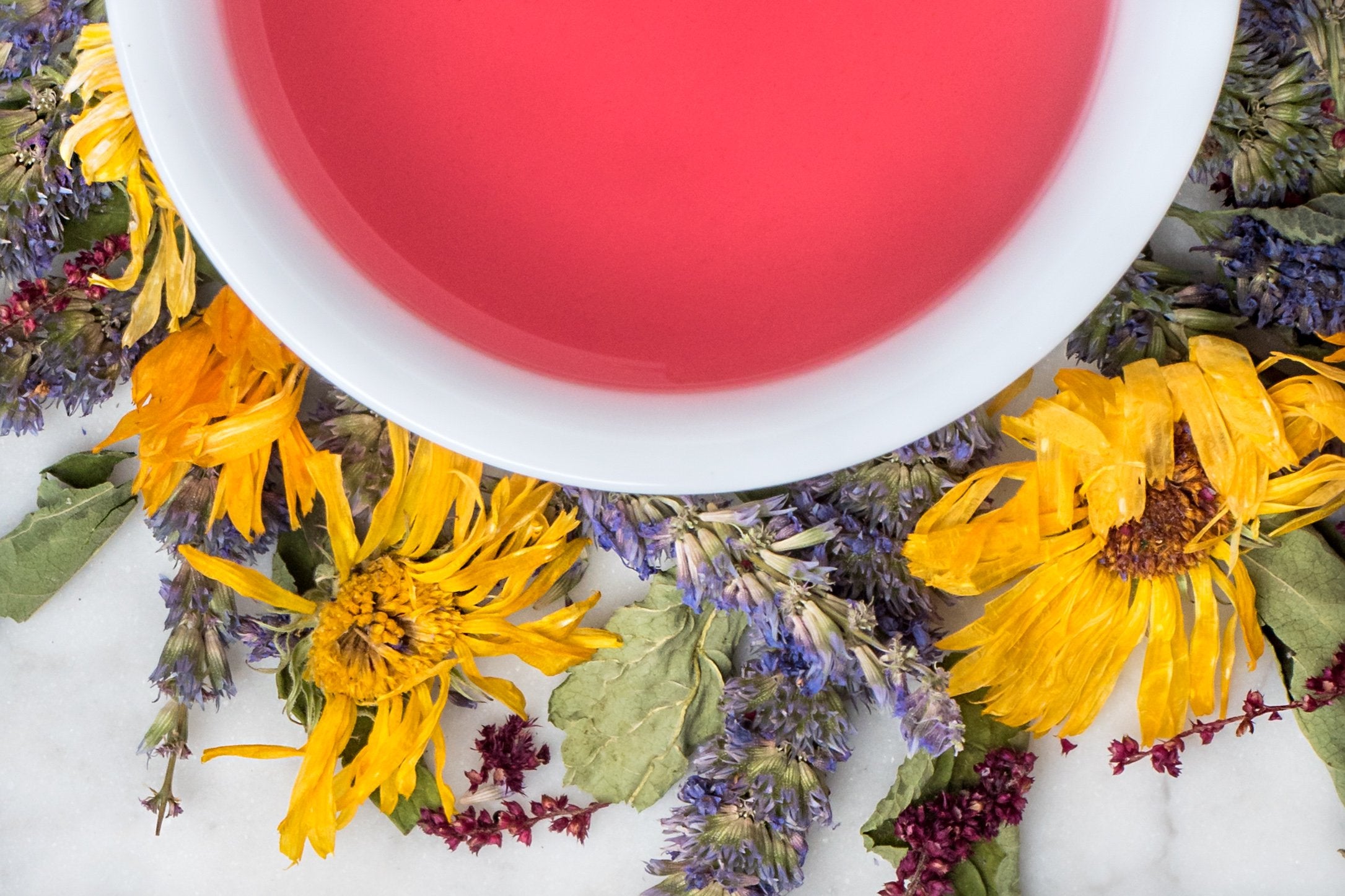 Tranquilité leaves and brewed Tea. Full calendula, amaranth and agastache dried flowers surround a cup of bright pink brewed herbal tea for relaxation. 