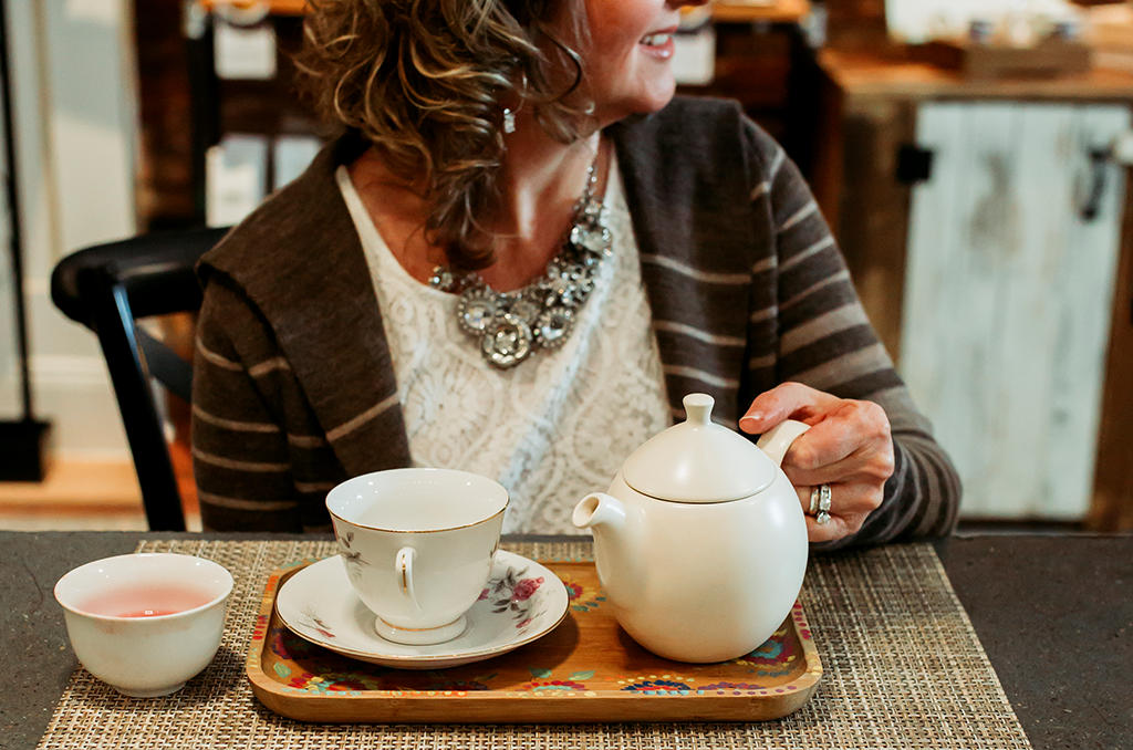 woman sitting at the tea bar at Saratoga Tea & Honey Co. with a teapot and vintage teacup on a wooden tray