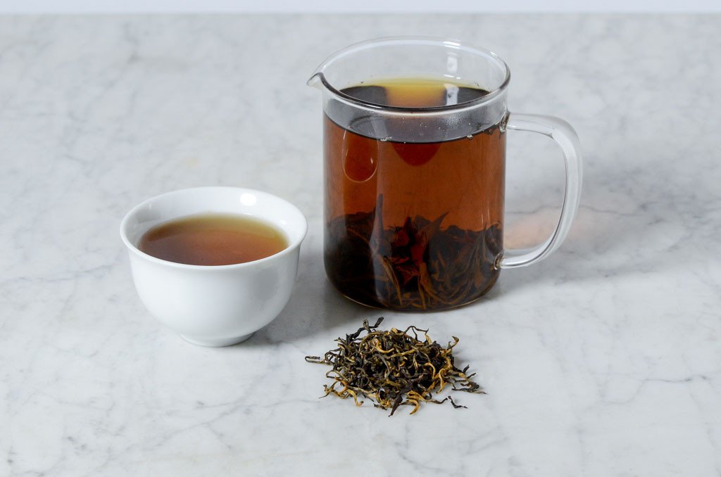 cup, infuser, and pile of yunnan da ye black loose leaf tea leaves