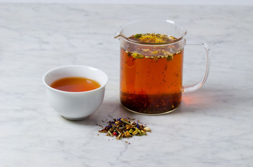 warm reddish brown infusion of cinnamon and citrus tea in a white cup and glass infuser