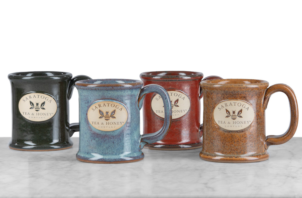 microwave, oven, and dishwasher safe green, blue, red, and sand colored stoneware bee mugs with saratoga tea and honey co logo