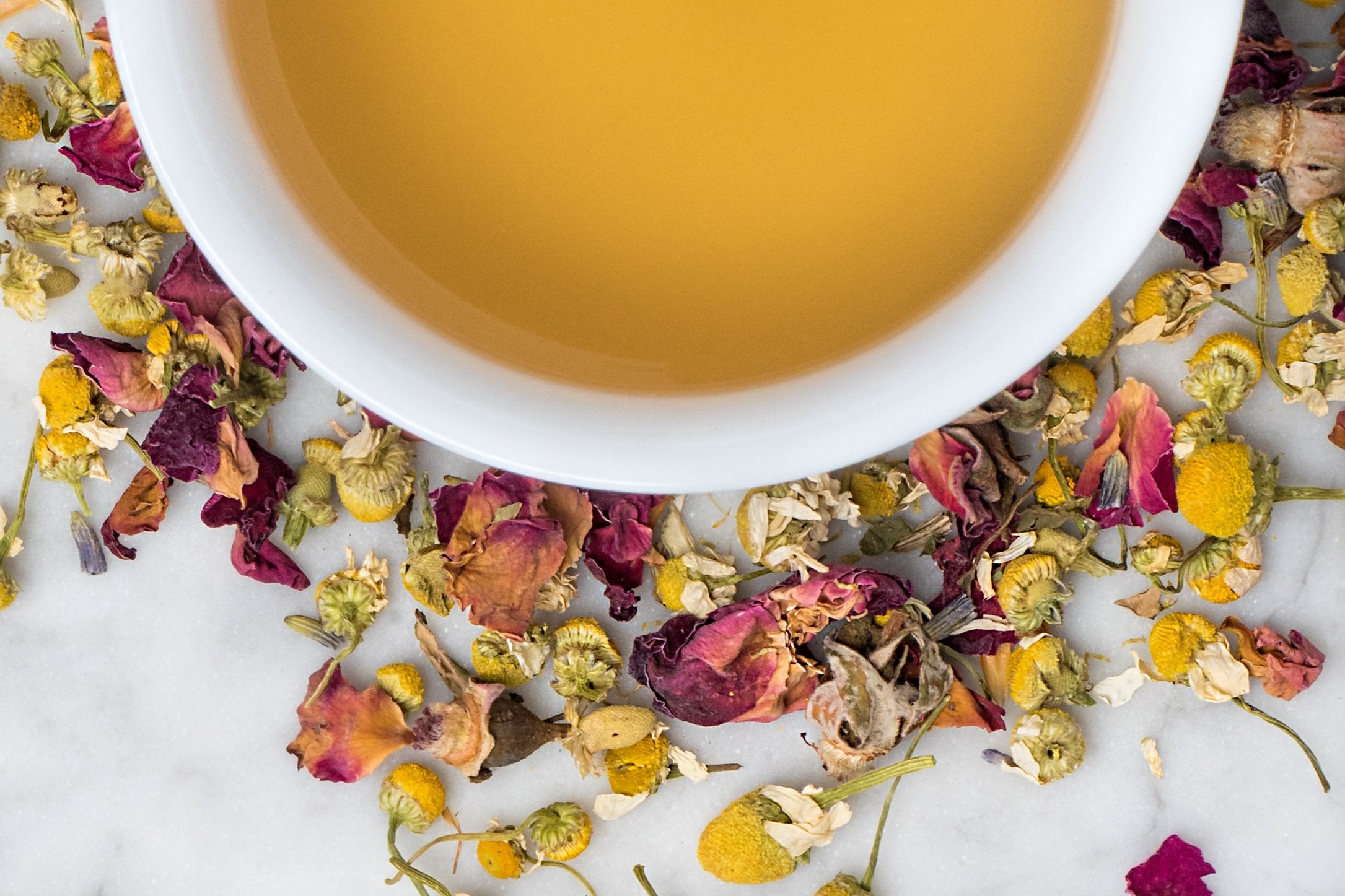 A Quiet Mind loose leaf herbal tea and brewed tea. Chamomile, rose, passionflower, valerian, and ashwagandha surround a cup of old-gold colored tea.