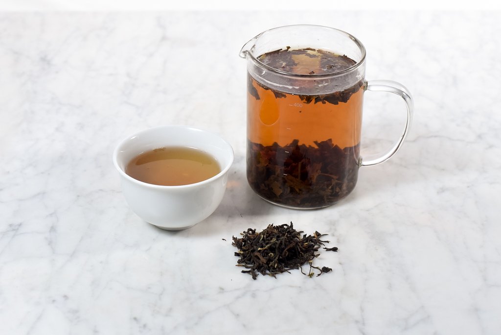 cup of darjeeling next to a glass beaker infuser of black tea and darjeeling loose tea leaves