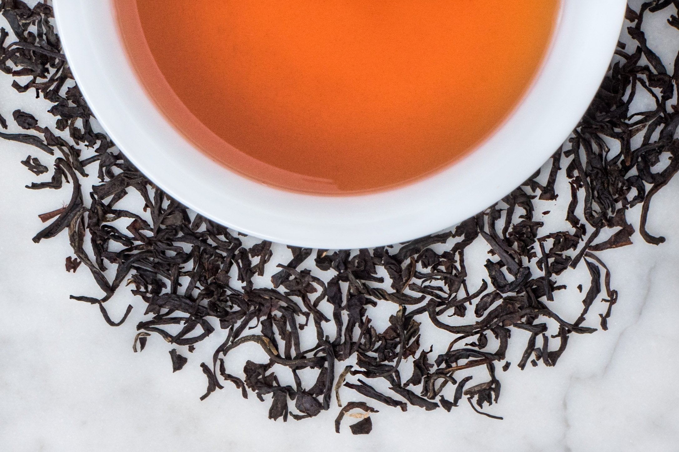 Fair Trade Earl Grey leaves and brewed tea. Thin, twisted black tea leaves surround a cup of russet-hued black tea.