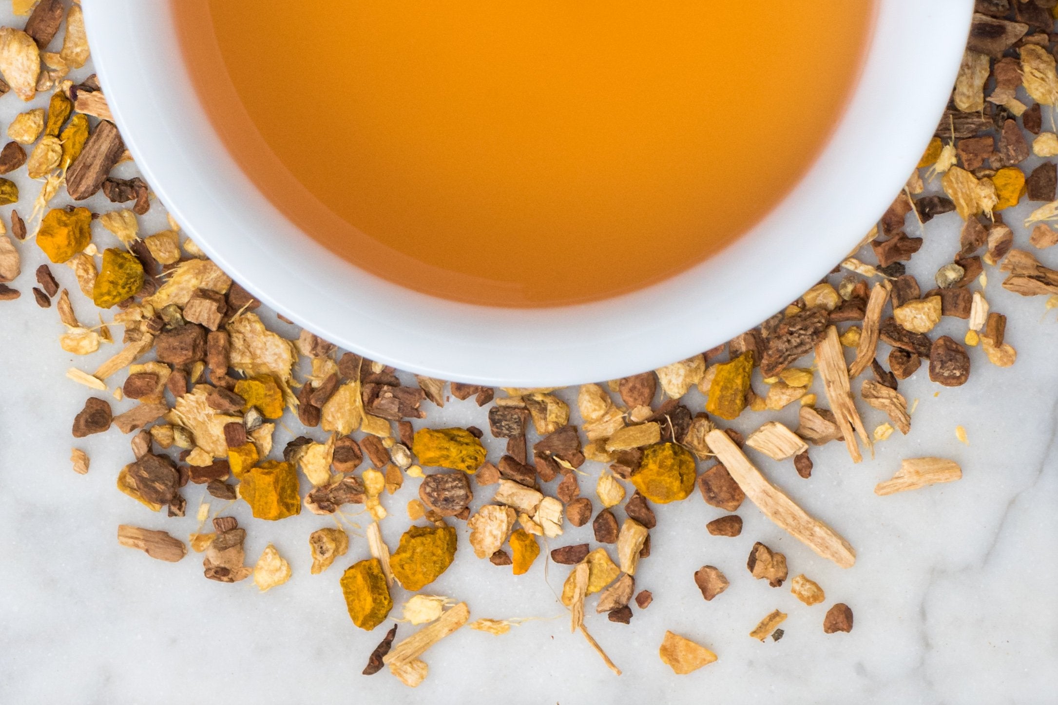 Fountain of Youth leaves and brewed tea. Small chunks of turmeric, cinnamon, and other spices surround a cup of amber-hued brewed tea.