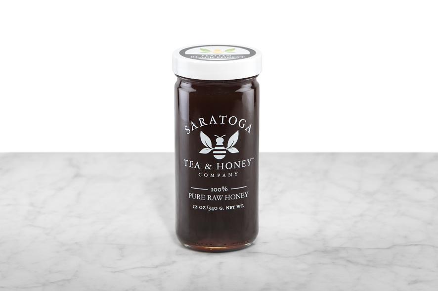 Dark-amber Italian Black Forest Honey displayed in a 12oz cylindrical glass jar with a white lid. The logo and the words: "100% Pure Raw Honey" are printed on the jar.