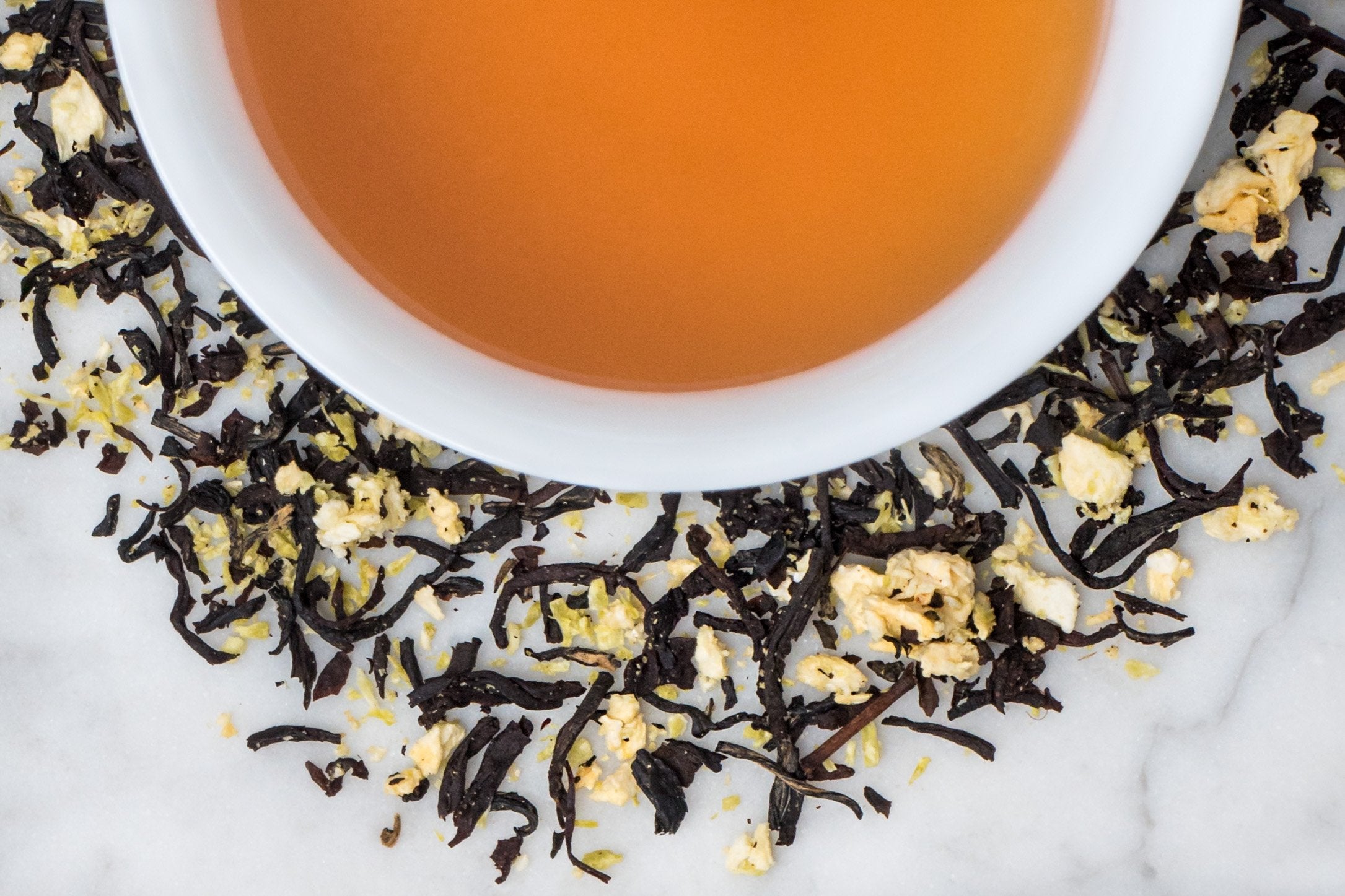 One Night in Rio leaves and brewed tea. Twisted black tea leaves with coconut and pineapple pieces surrounds a cup of medium-brown brewed tea.