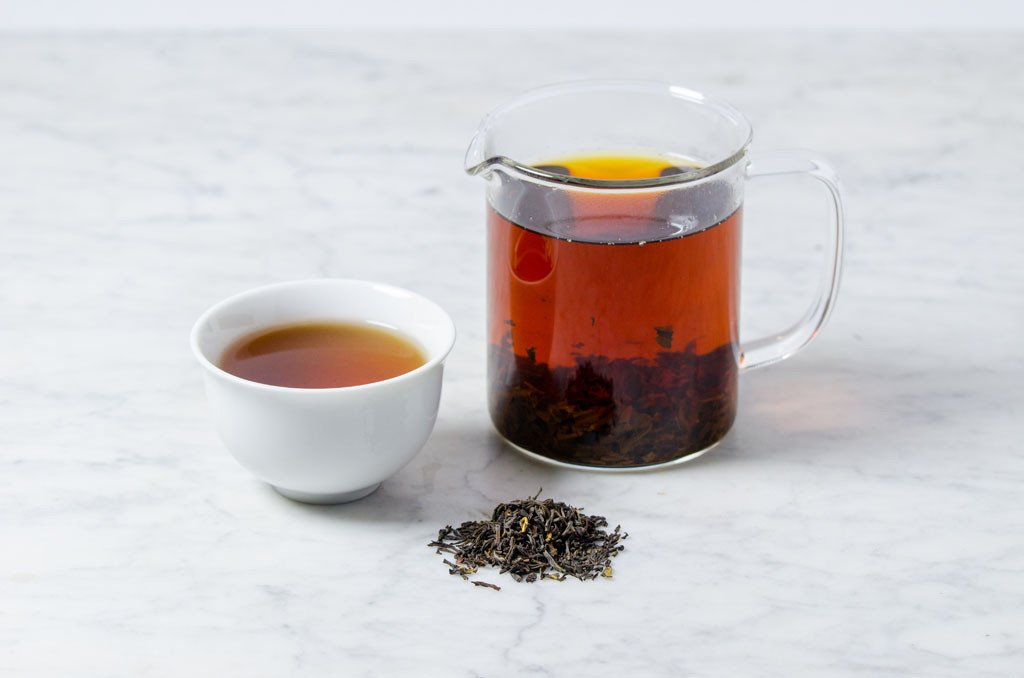 Deep umber infusion of Russian Caravan black tea presented side-by-side in white cup and glass infuser with a small scattering of black tea leaves