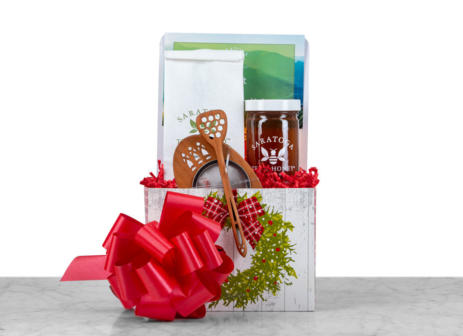 small tea and honey gift basket in holiday motif with honey, wooden dipper, tea, and wooden tea infuser