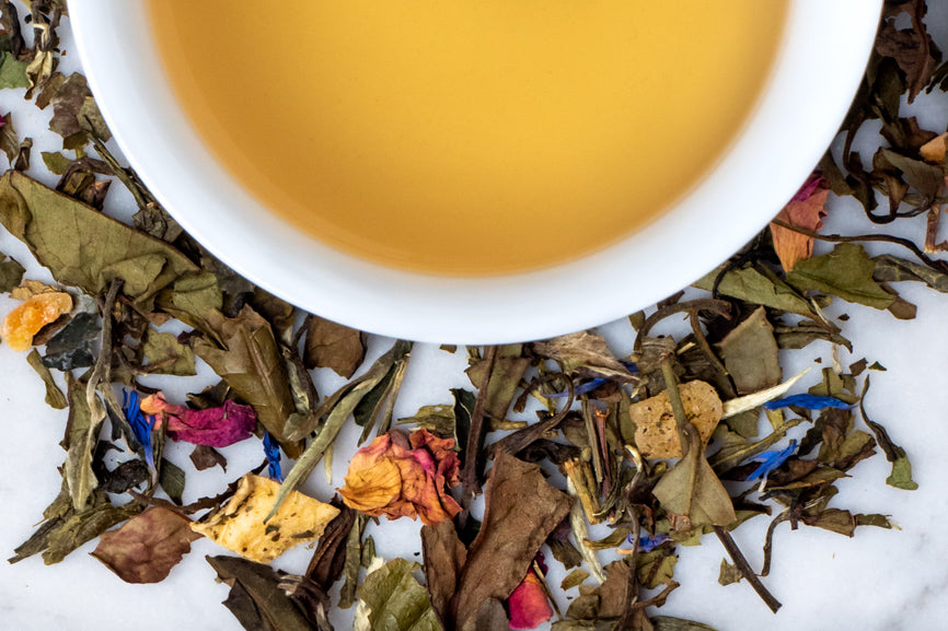 Sweet White Peach leaves and brewed tea. White tea, rose petals, and dried peach surround a cup of light yellow brewed tea.