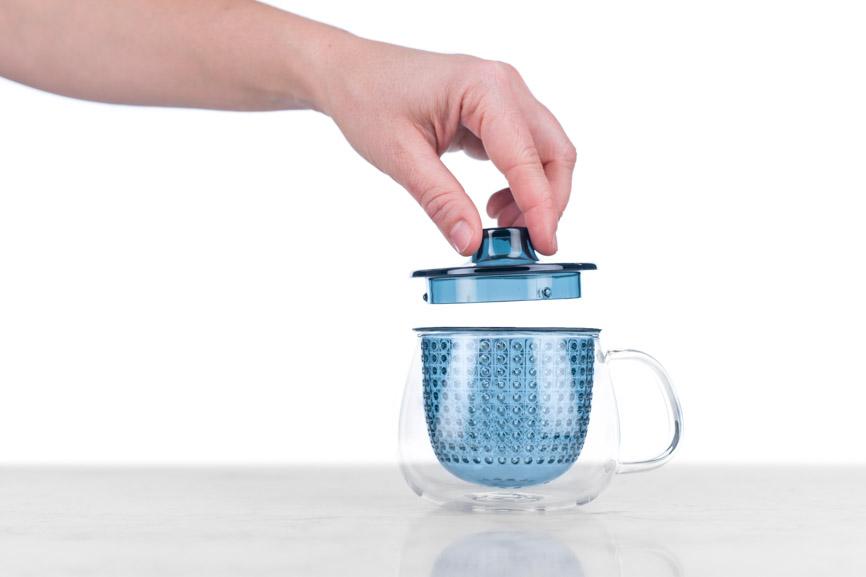 hand putting lid on glass tea brew-in mug with blue infuser and lid