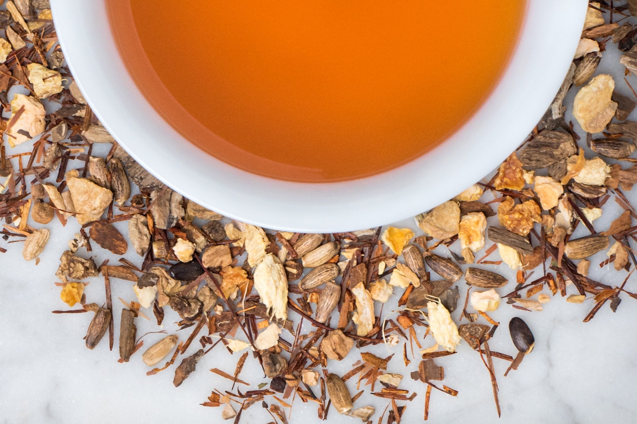 Teatoxify leaves and brewed tea. A granola-like collection of roots and leaves surrounds a cup of russet-hued brewed herbal tea.
