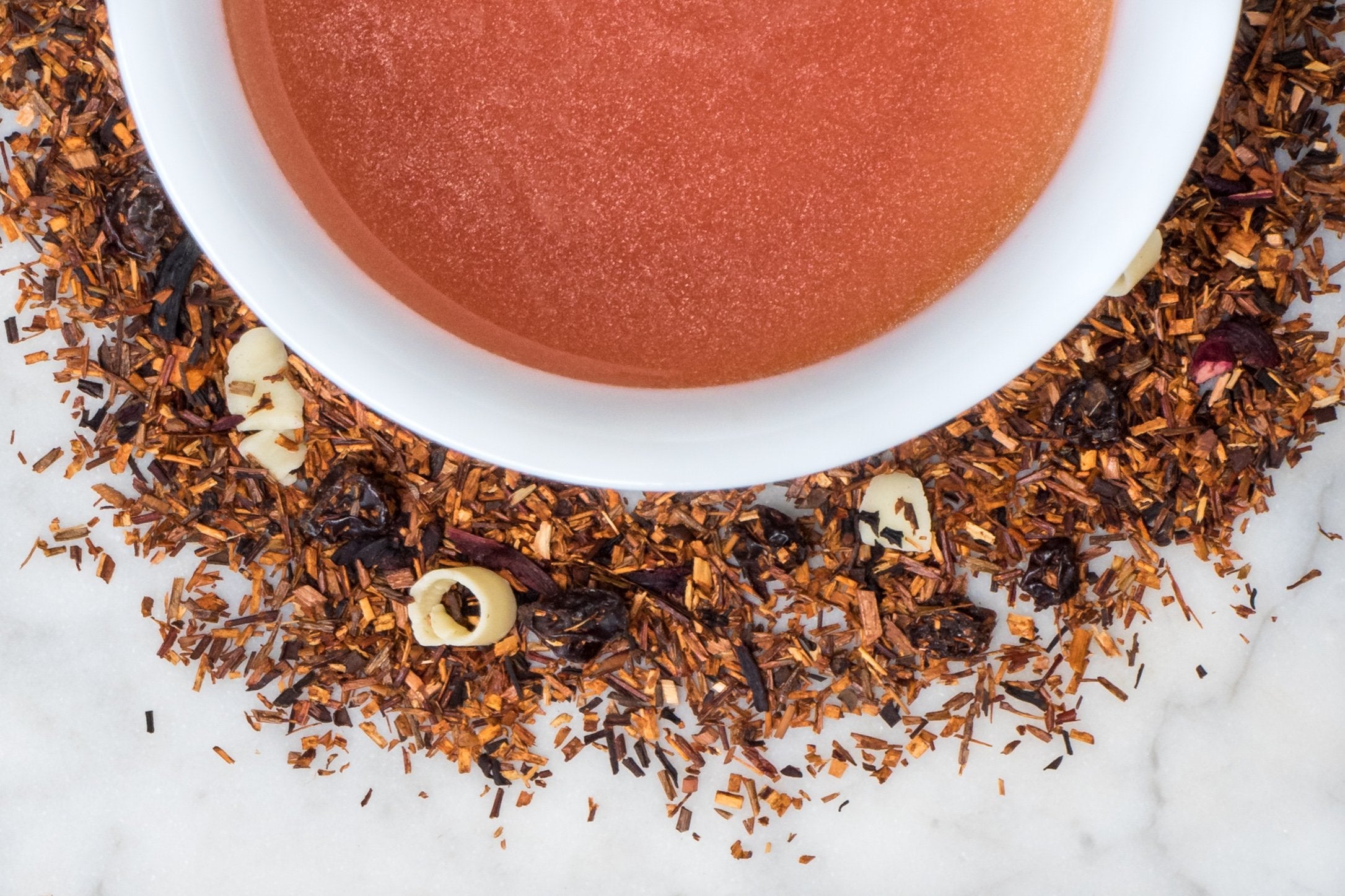 loose leaf berry and white chocolate rooibos herbal tea surrounding a white cup of brewed tea