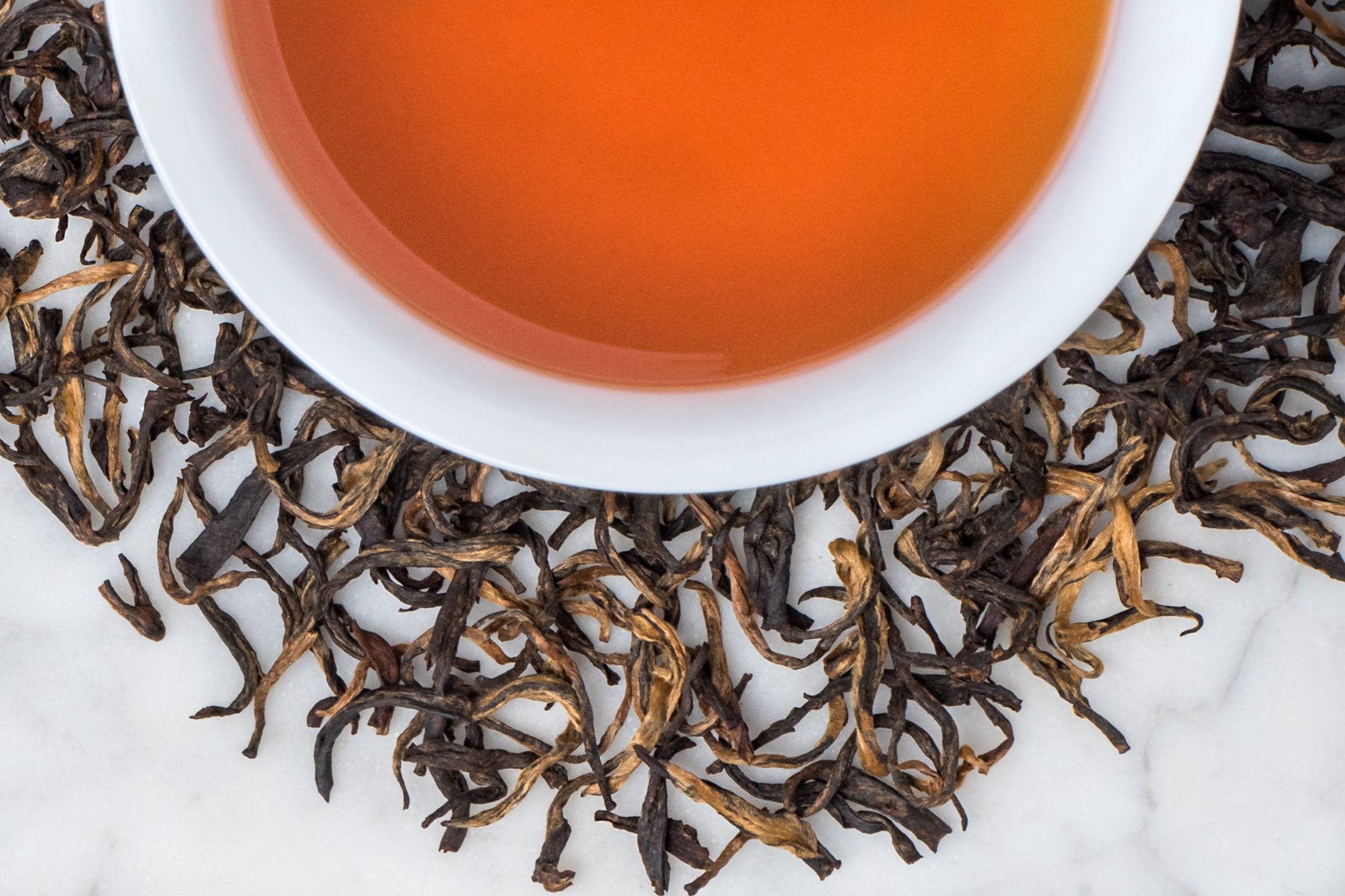 Black Leaves Twisted With Golden Buds Surround A Cup of Perfectly Steeped Yunnan Black Tea